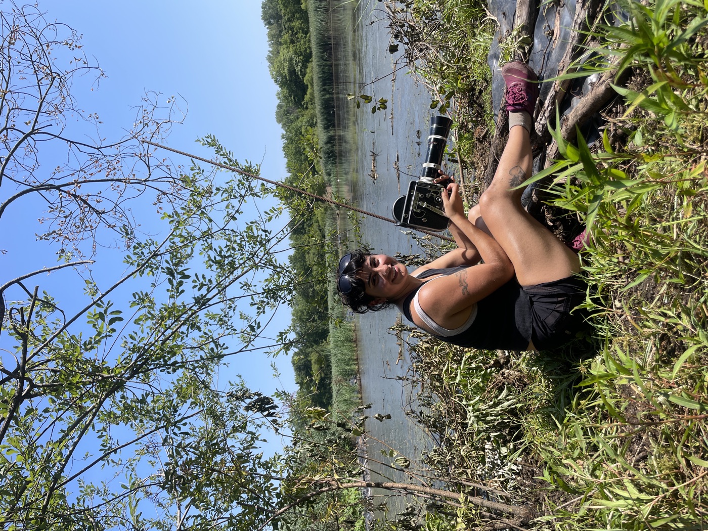 Olivia Acuña filming with a 16mm camera at the edge of a reservoir